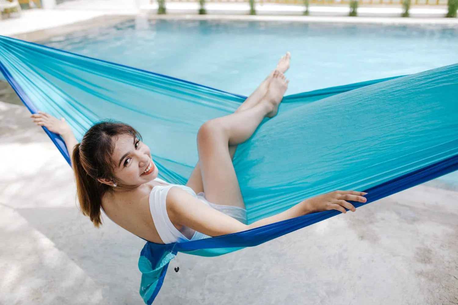Smiling woman relaxing on a blue hammock by a swimming pool outdoors