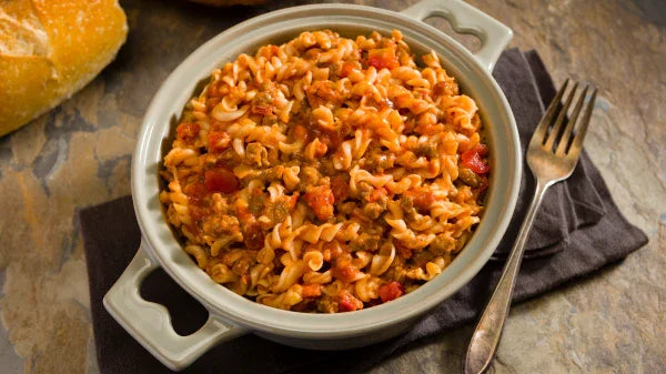 Bowl of rotini pasta with tomato sauce and ground meat, served with bread and fork