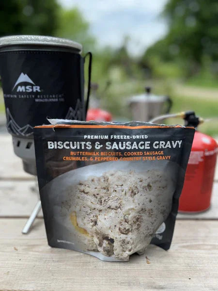 Biscuits and sausage gravy freeze-dried meal on picnic table with camping stove outdoors