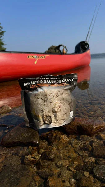 Biscuits and sausage gravy freeze-dried meal on lake shore with red fishing kayak