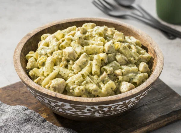 Chicken pesto pasta in a wooden bowl on a rustic board, creamy sauce visible