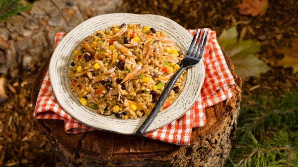 Plate of sweet pork rice with beans and corn on a stump, outdoor picnic setting