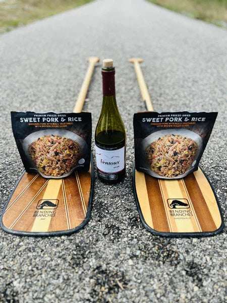 Sweet pork and rice freeze-dried meal packs, wine bottle, and paddles on a road