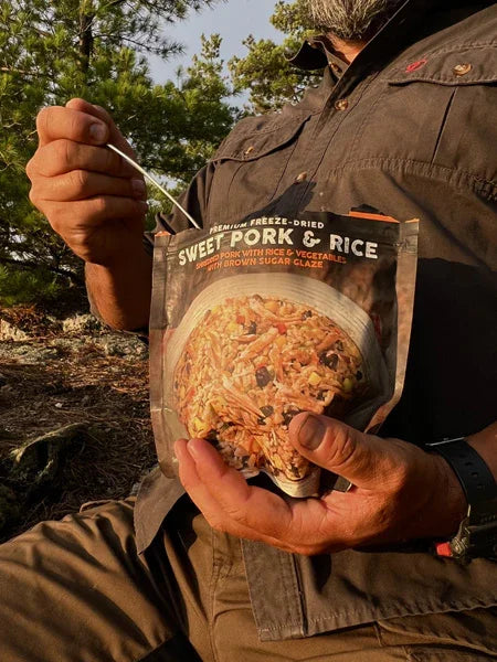 Man eating premium freeze-dried sweet pork and rice outdoors in nature