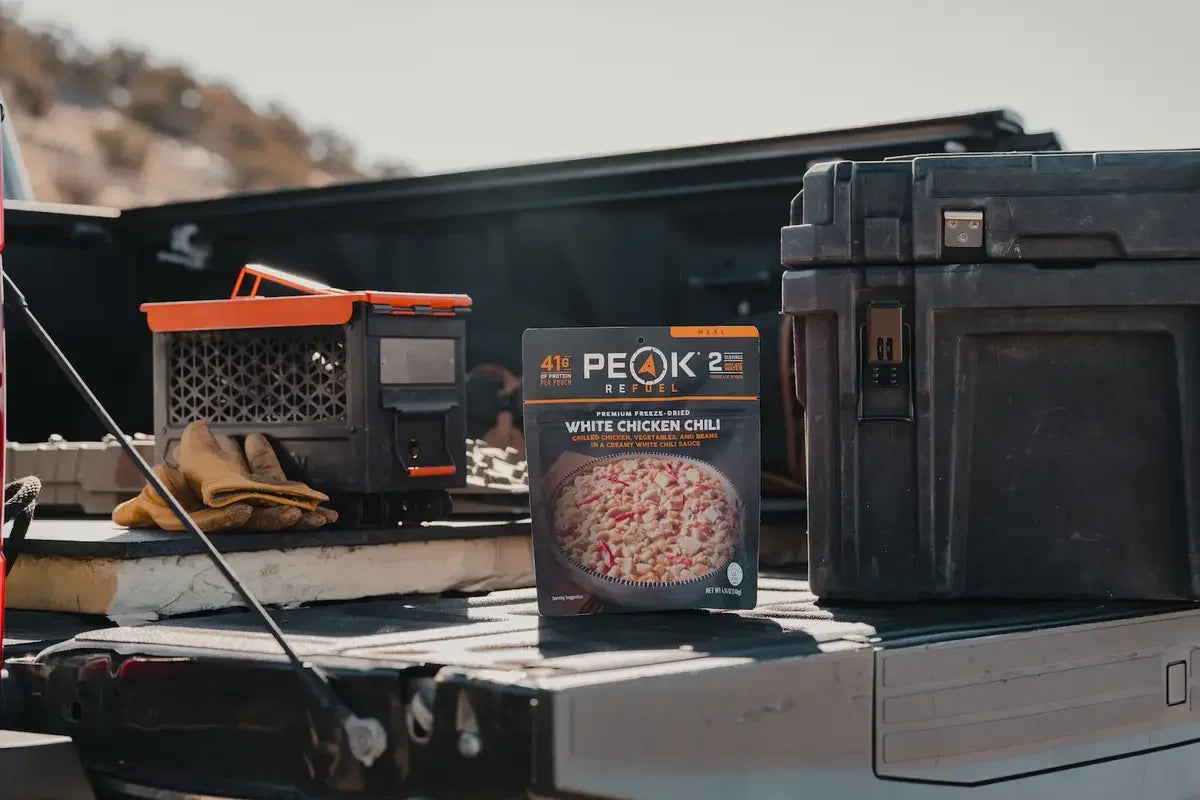 Peak Refuel White Chicken Chili freeze-dried meal on truck bed outdoors with gear boxes