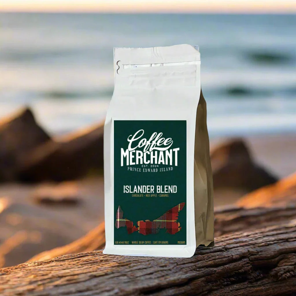 Coffee Merchant Islander Blend coffee bag on driftwood by the beach with ocean in background