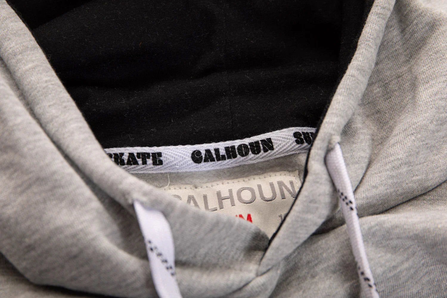 Close-up of grey hoodie hood with CALHOUN label and white drawstrings