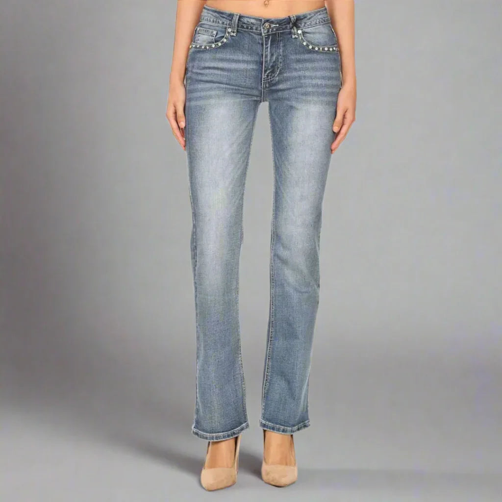 Women's light wash bootcut jeans with rhinestone pockets, modeled on gray background
