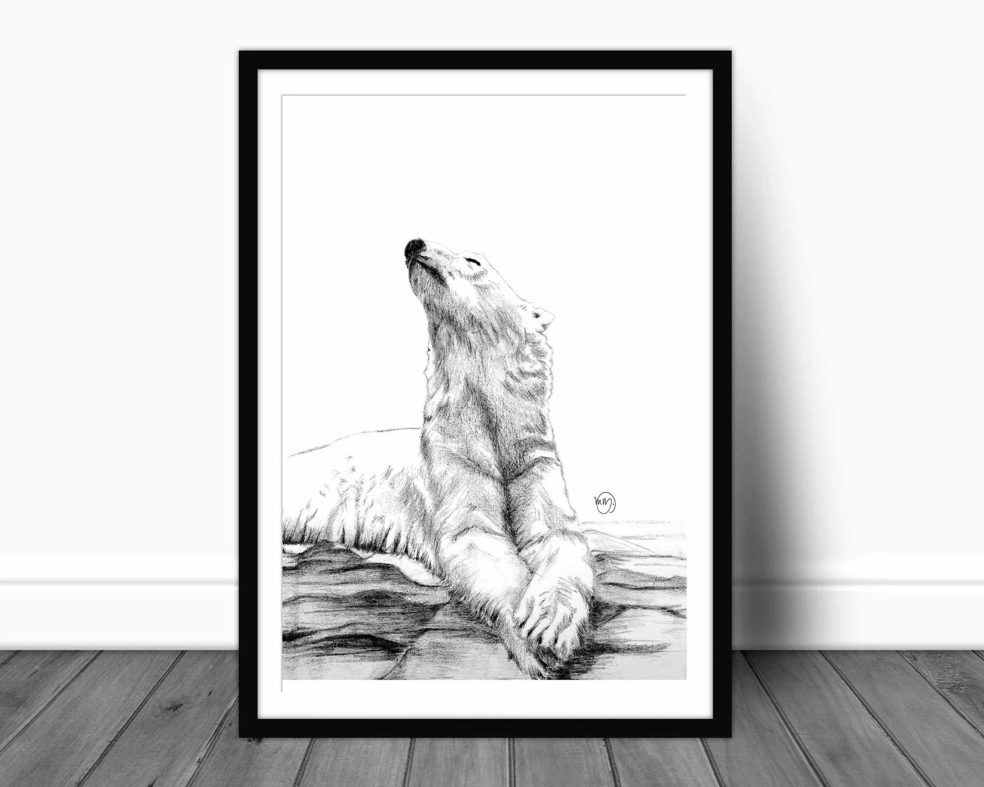 Black and white sketch of a polar bear sunbathing, framed and displayed on a wooden floor.