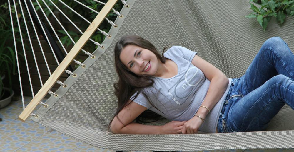 Woman relaxing on outdoor hammock, smiling, wearing jeans and t-shirt, patio and plants visible