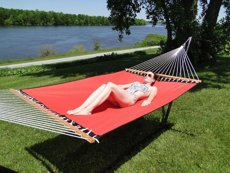 Woman relaxing on a red poolside hammock outdoors near a lake on a sunny day