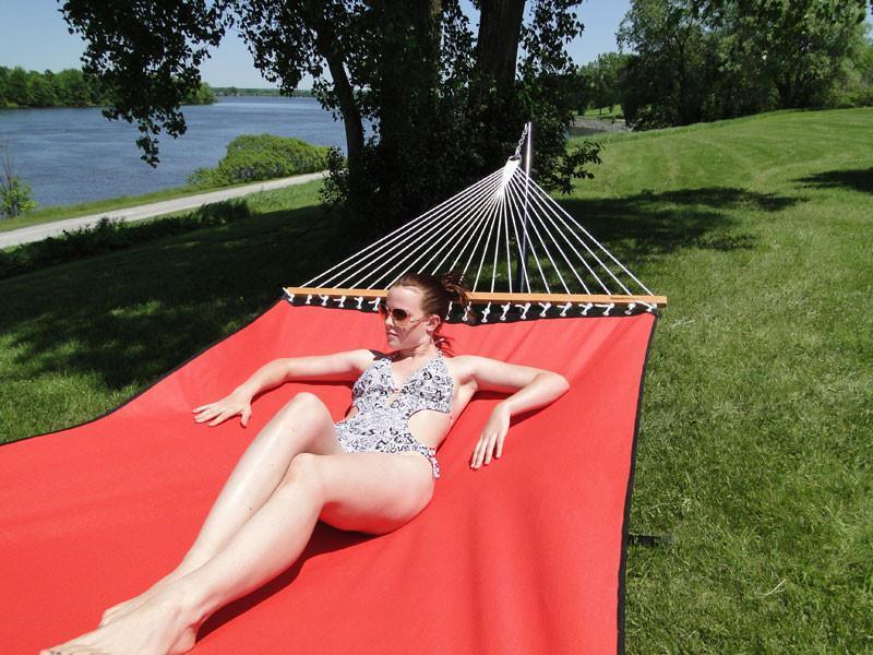 Woman relaxing on a red hammock by a riverside in a grassy, sunny outdoor setting