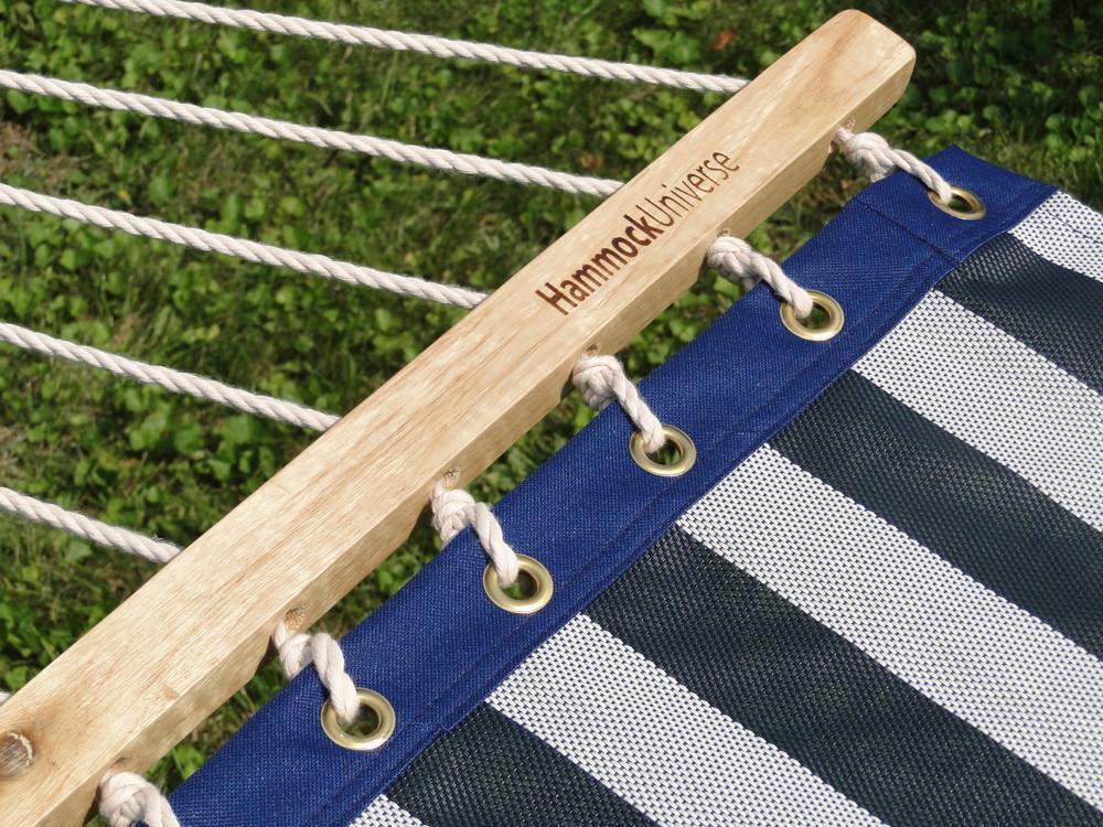 Blue and white striped hammock with wooden spreader bar outdoors on grass