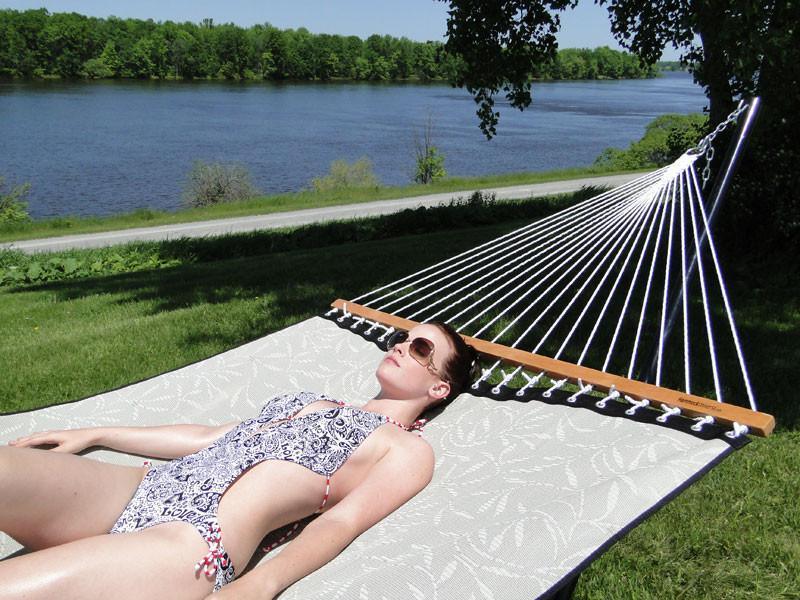 Woman relaxing on a hammock by a lake on a sunny day with green trees in the background