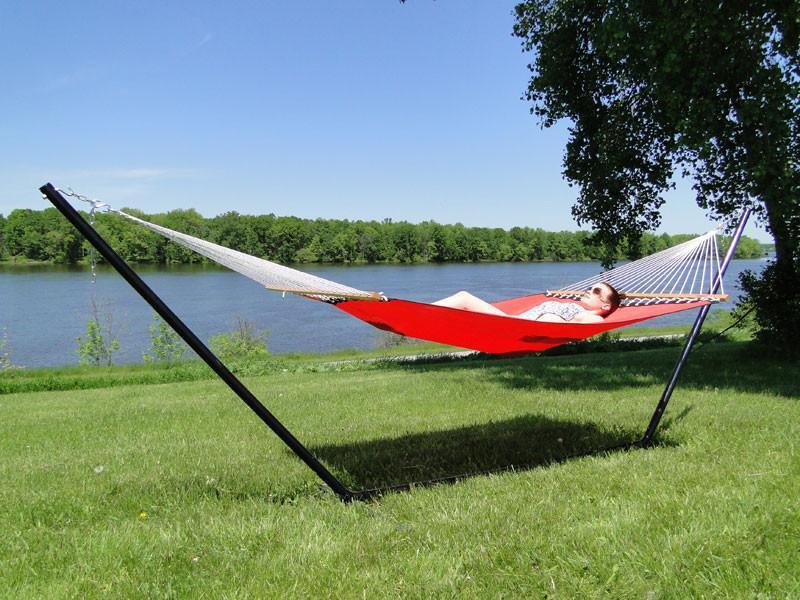 Woman relaxing on a red hammock with metal stand by a lakeside on green grass, sunny day