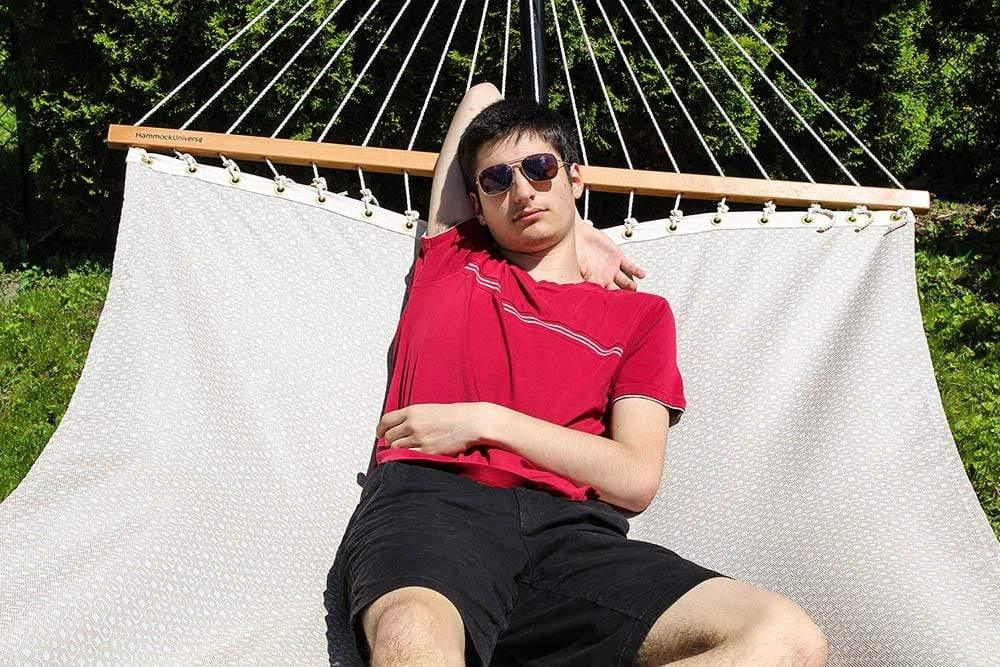 Man relaxing on a sand-colored double hammock outdoors, wearing sunglasses