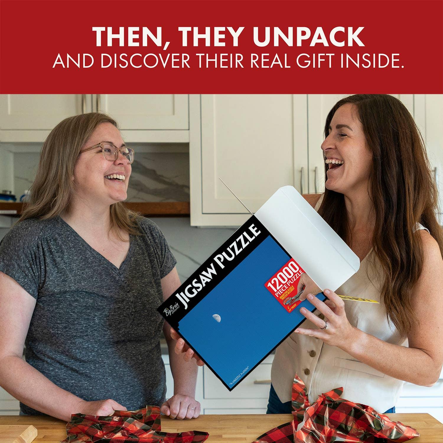 Two women in a kitchen laughing while unboxing a 12,000 piece jigsaw puzzle gift.