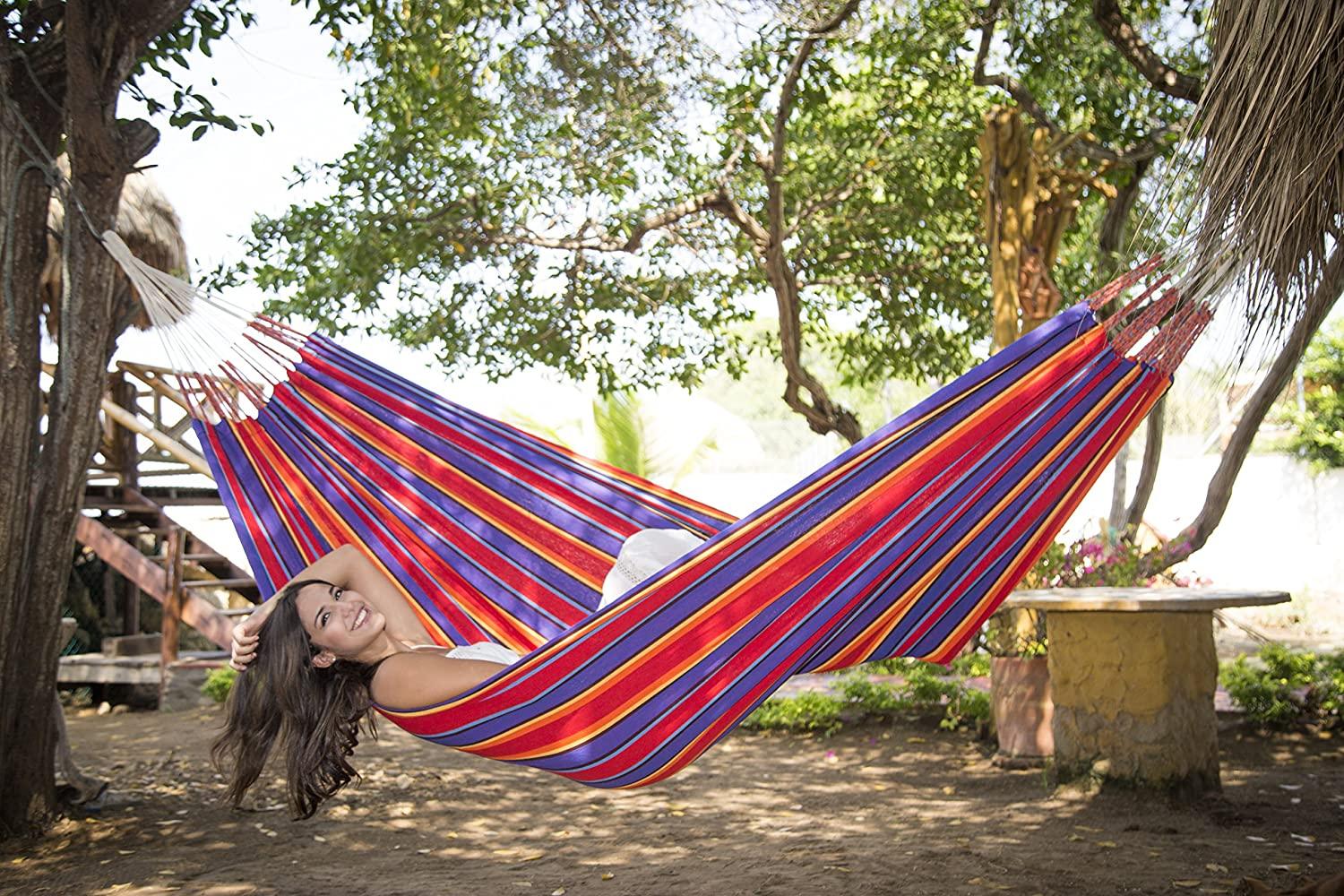 Woman relaxing in a colorful striped Yagua Morada hammock outdoors under trees