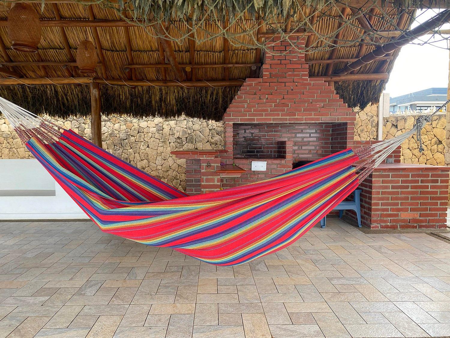 Colorful striped hammock hanging near a brick barbecue under a thatched roof patio