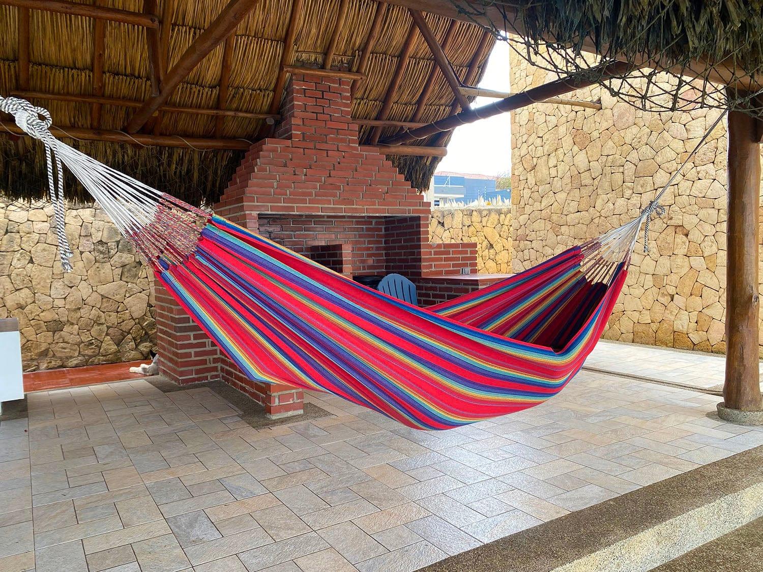 Colorful striped hammock hanging under thatched roof beside brick grill and stone wall