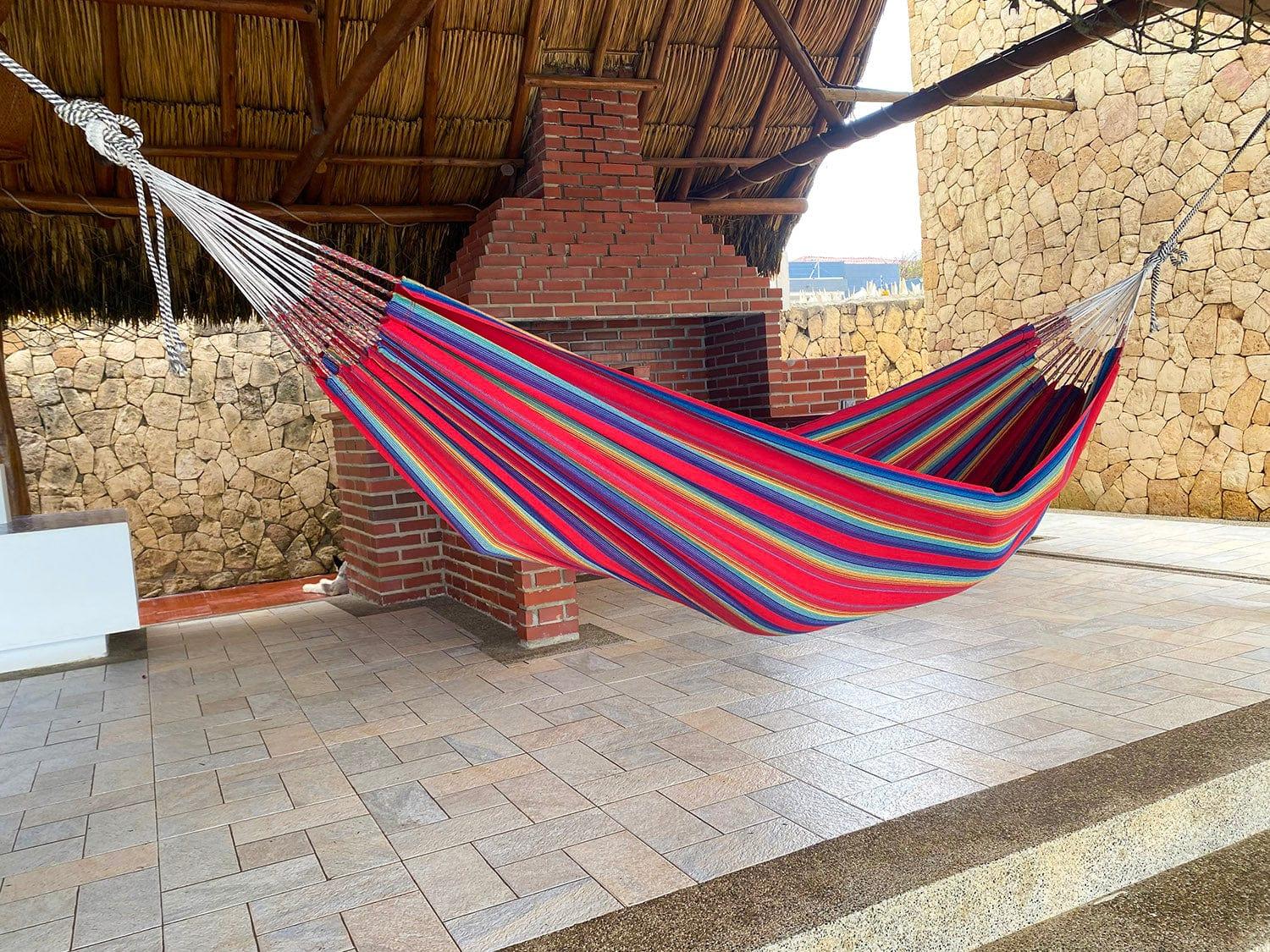 Colorful striped hammock hanging under thatched roof patio with brick and stone walls