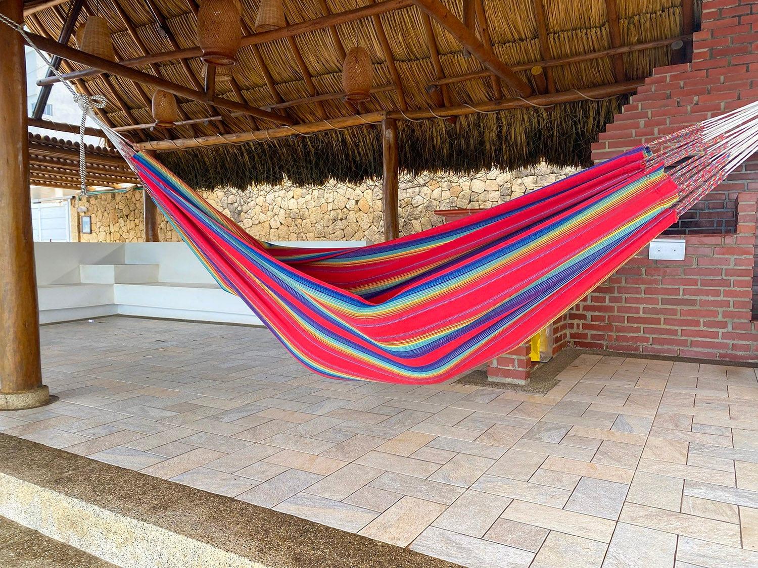 Colorful striped hammock in outdoor patio with brick wall and thatched roof