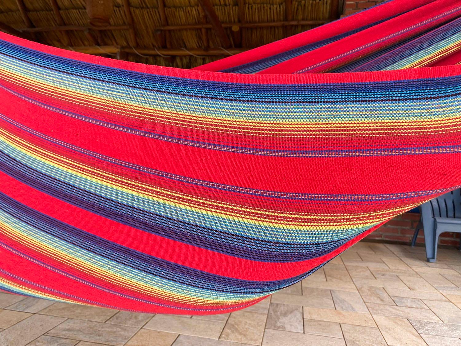 Colorful striped hammock with red, yellow, and blue under thatched roof on tiled patio