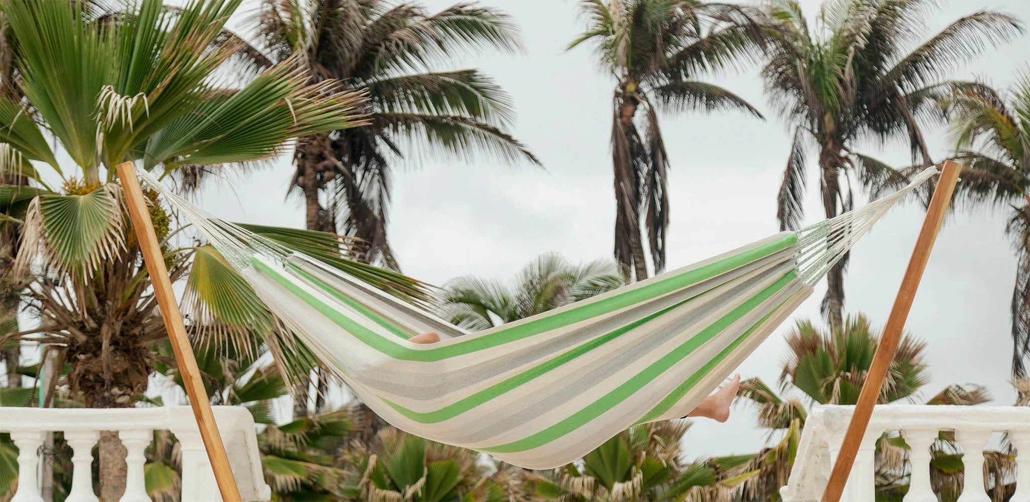 Green, grey, and white striped Brazilian hammock outdoors with palm trees in the background