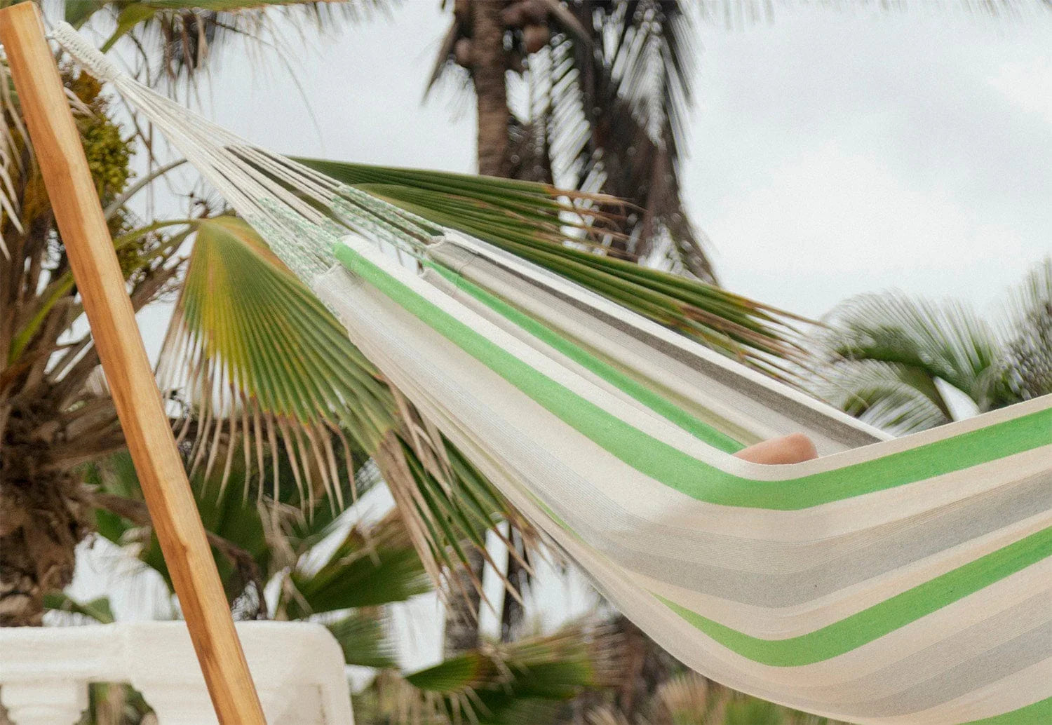 Green, grey, and white striped Brazilian hammock outdoors with palm trees in background