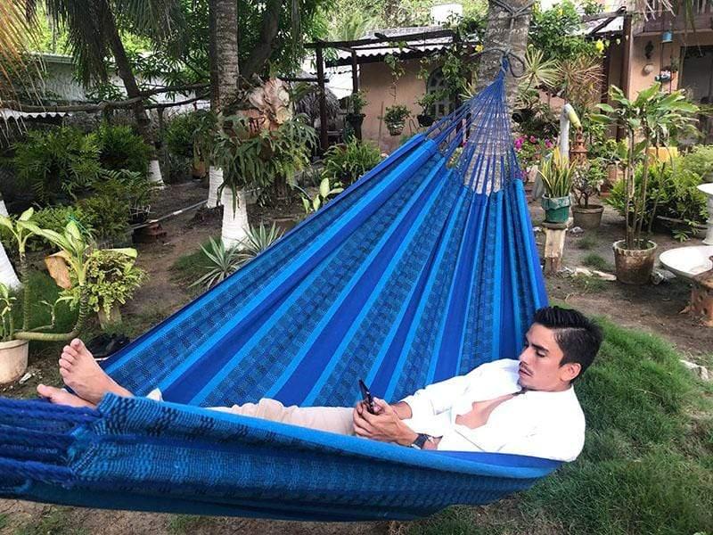 Man relaxing in blue and black Brazilian double hammock in lush garden setting