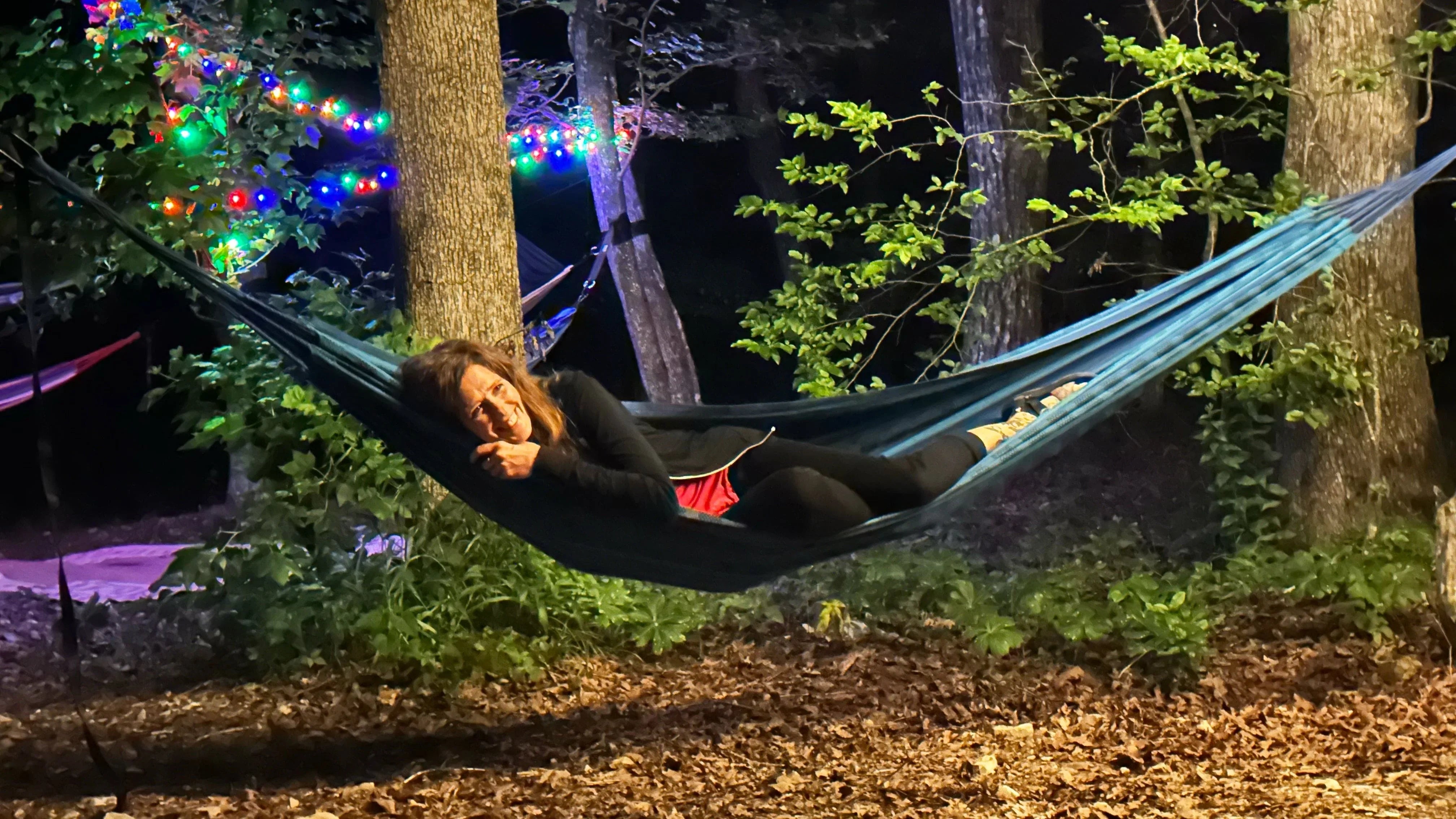 Woman relaxing in a hammock at night in the woods, with string lights and trees, Hot Springs AR