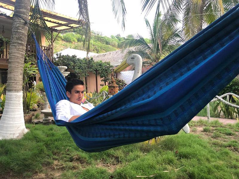 Man relaxing in a blue and black Brazilian double hammock outdoors with palm trees