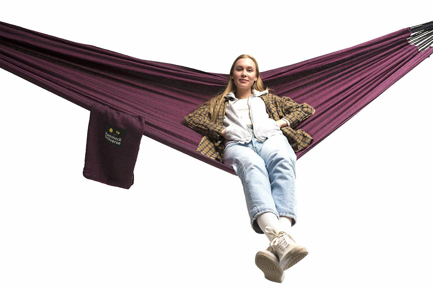 Woman relaxing in a purple Brazilian double hammock with Hammock Universe logo bag