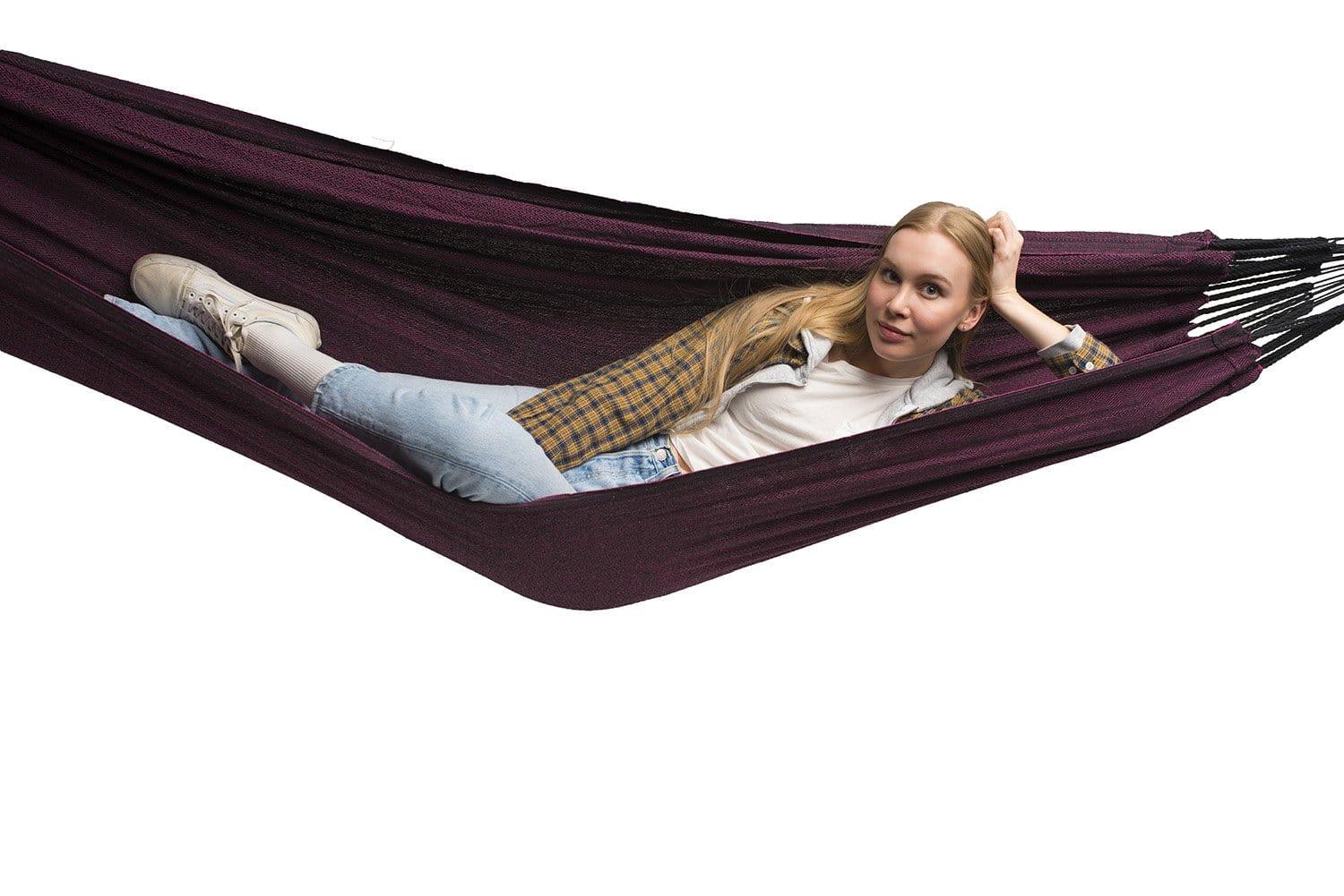 Woman relaxing in a purple and black Brazilian double hammock on a white background
