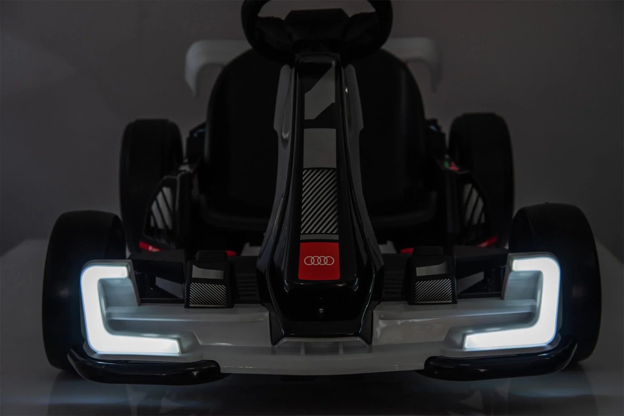 Front view of black Audi electric go-kart with LED headlights in a dark setting