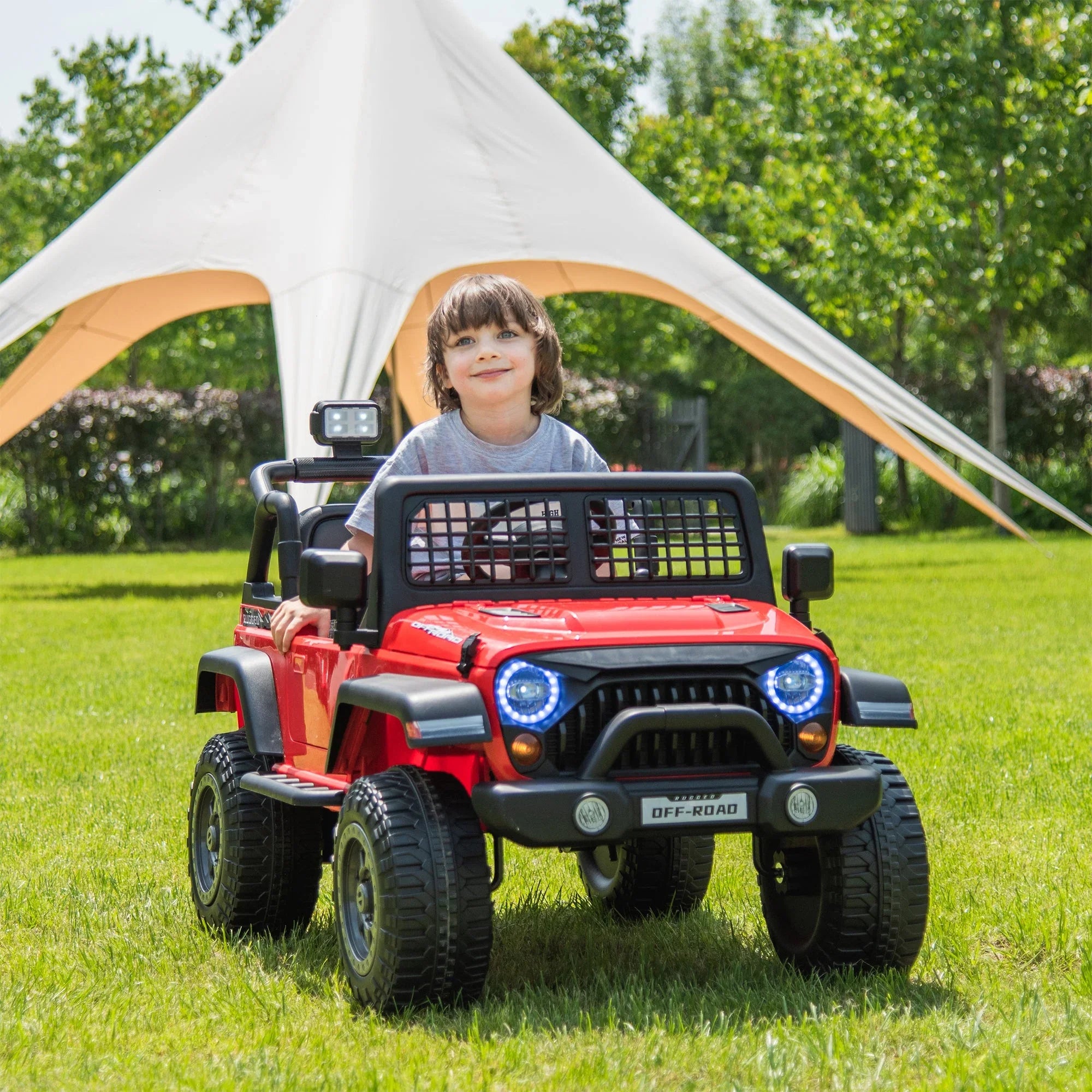Child riding red electric toy Jeep on grass under canopy, outdoor kids ride-on car