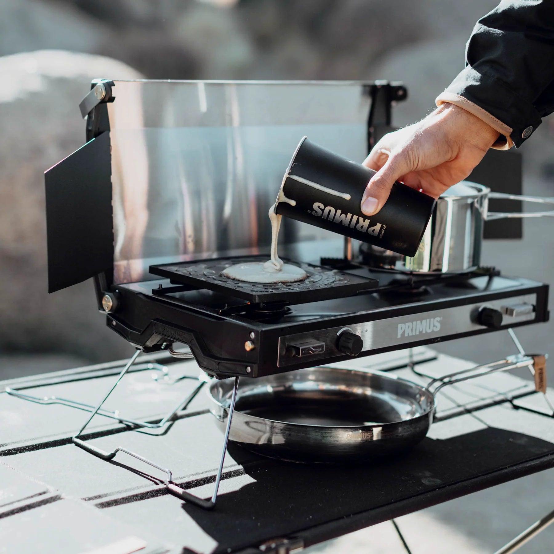 Pouring batter on Primus campfire griddle plate outdoor camping stove setup