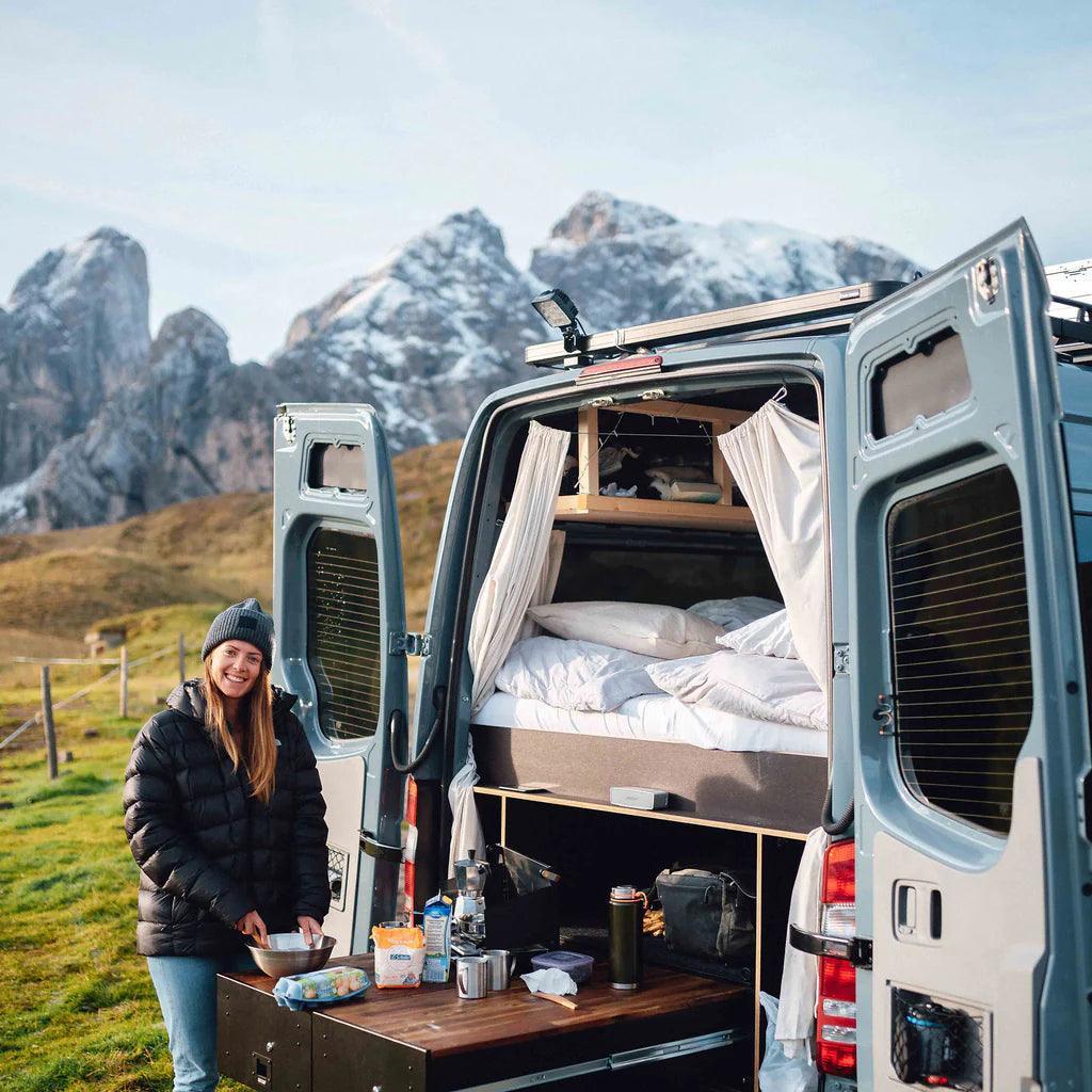 Woman cooking by camper van with camp kitchen in scenic mountain outdoor setting