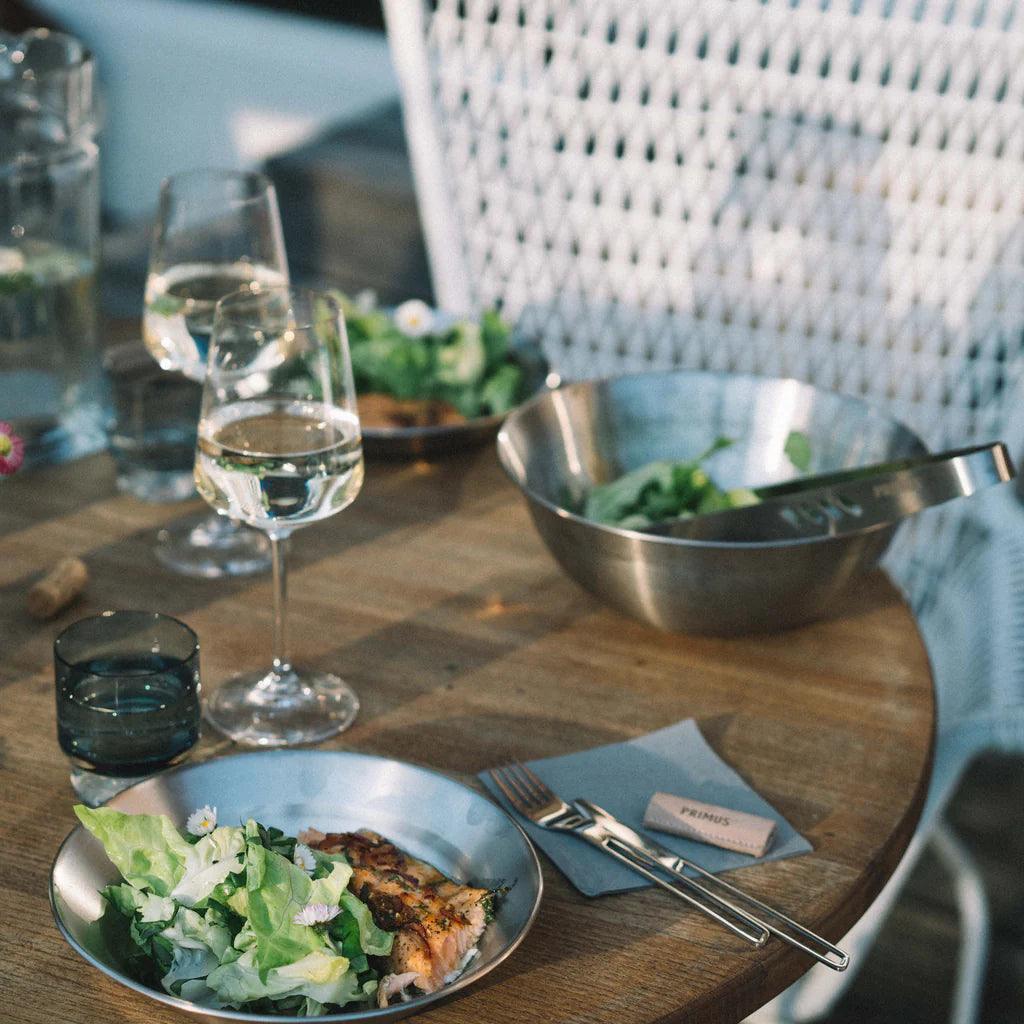 Primus Campfire Serving Kit with salad and grilled fish on outdoor wooden table, glass of wine