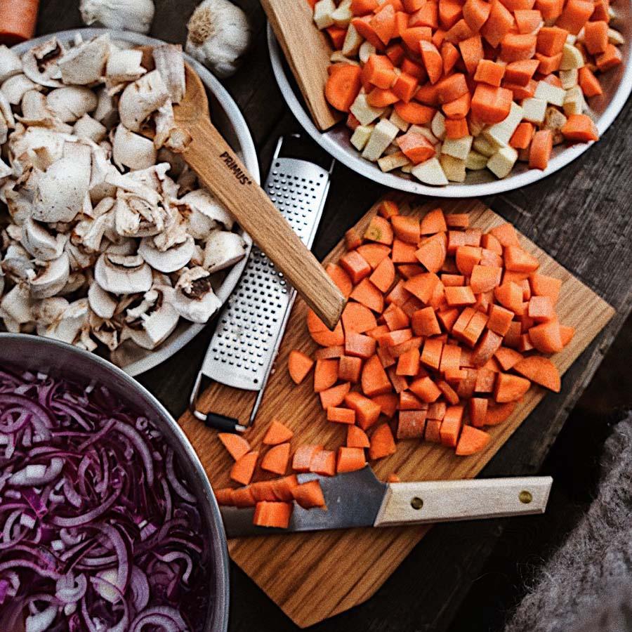 Chopped vegetables, Primus grater, and wooden utensils on a rustic outdoor table.