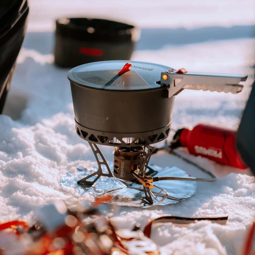 Primus camping stove with pot set on snow, outdoor winter campsite scene