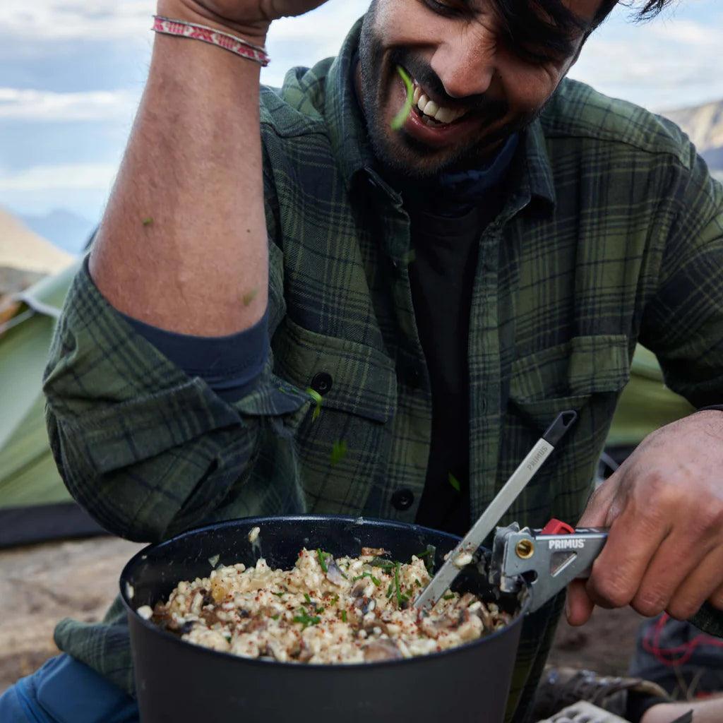 Camper cooking outdoors with Primus PrimeTech pot set at campsite