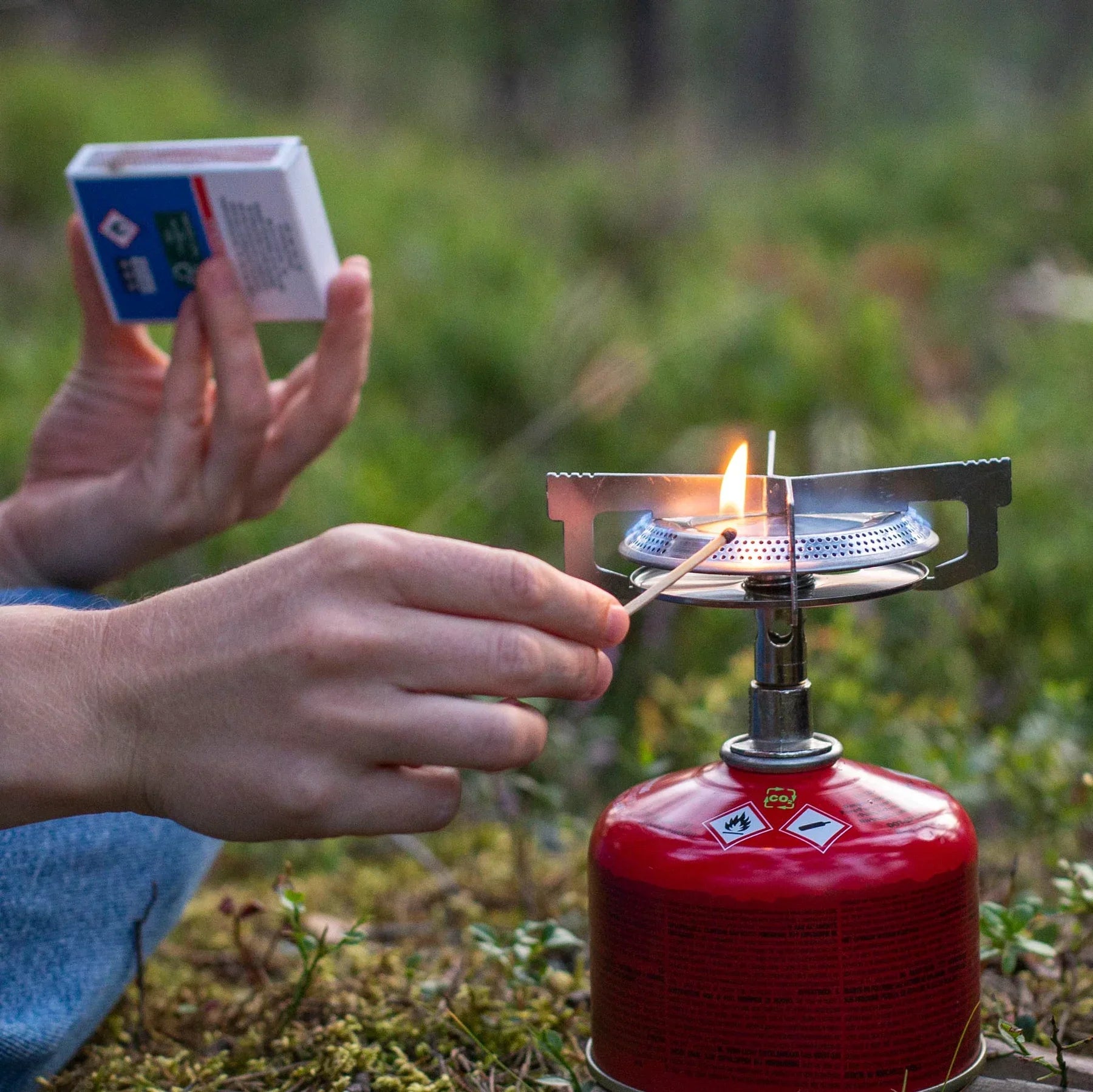 Lighting a portable camping gas stove outdoors with a match in a green forest setting