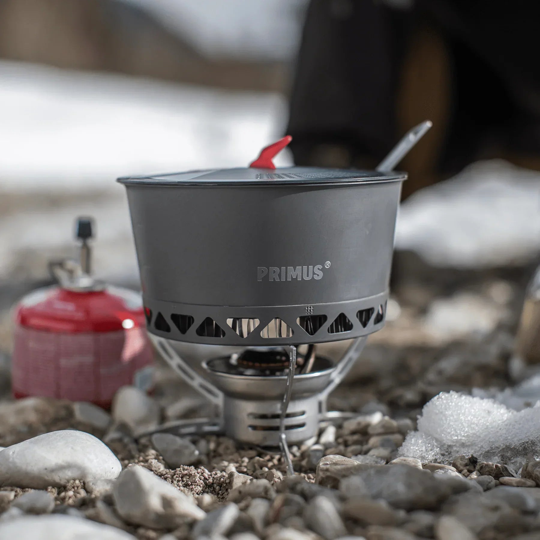 Primus portable camping stove and pot on rocky snowy ground outdoors