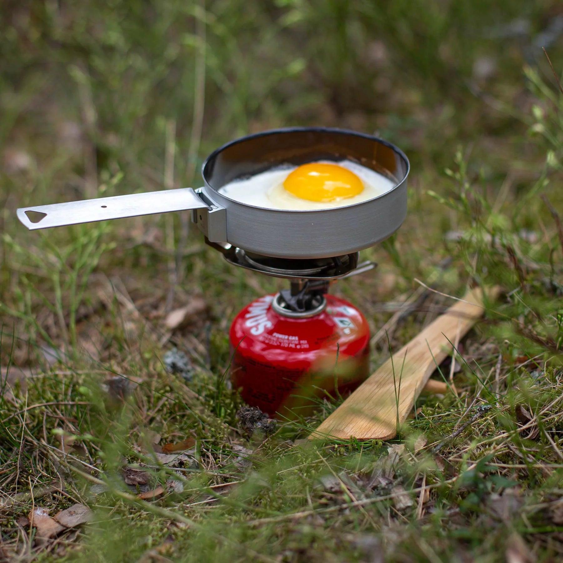 Primus Essential Trail Stove cooking a fried egg outdoors on grass