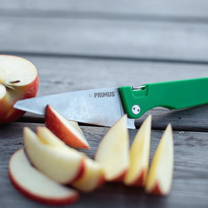 Primus Fieldchef pocket knife with green handle slicing apple on wooden surface
