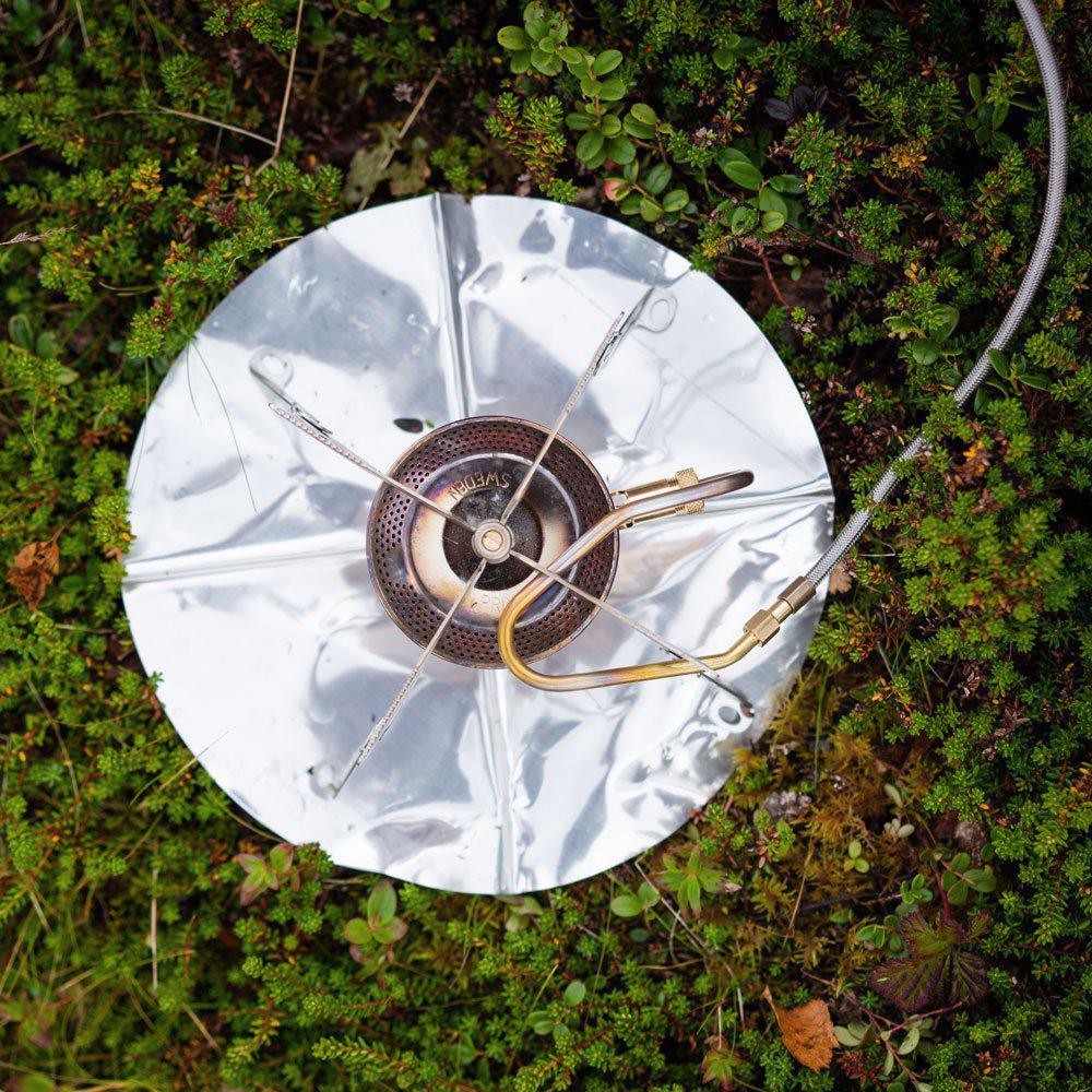 Outdoor camping stove with metal windscreen on green mossy ground, top view