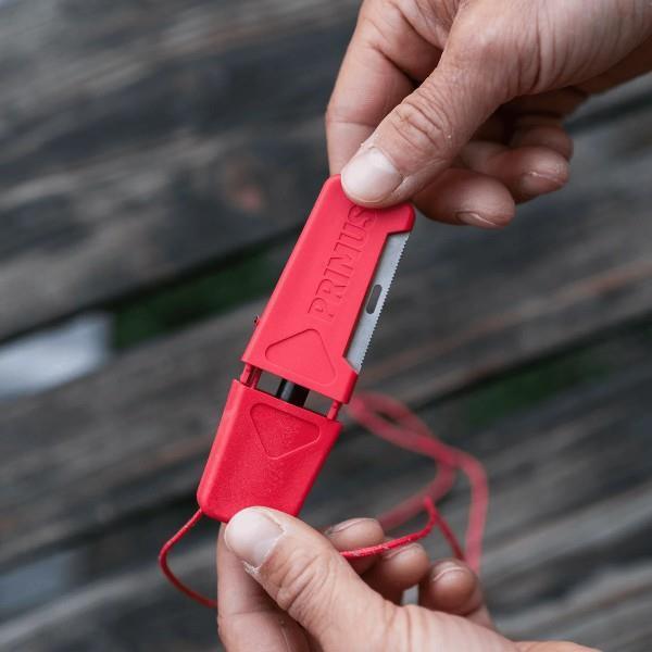 Hands holding a red Primus outdoor survival knife with a plastic sheath on wood background