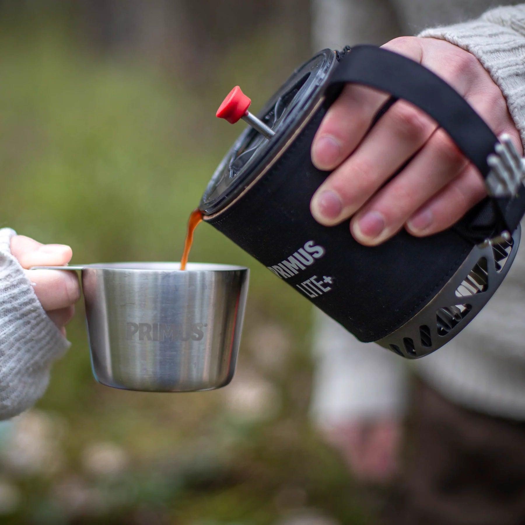 Pouring coffee from Primus Lite+ outdoor stove into Primus stainless steel mug outdoors