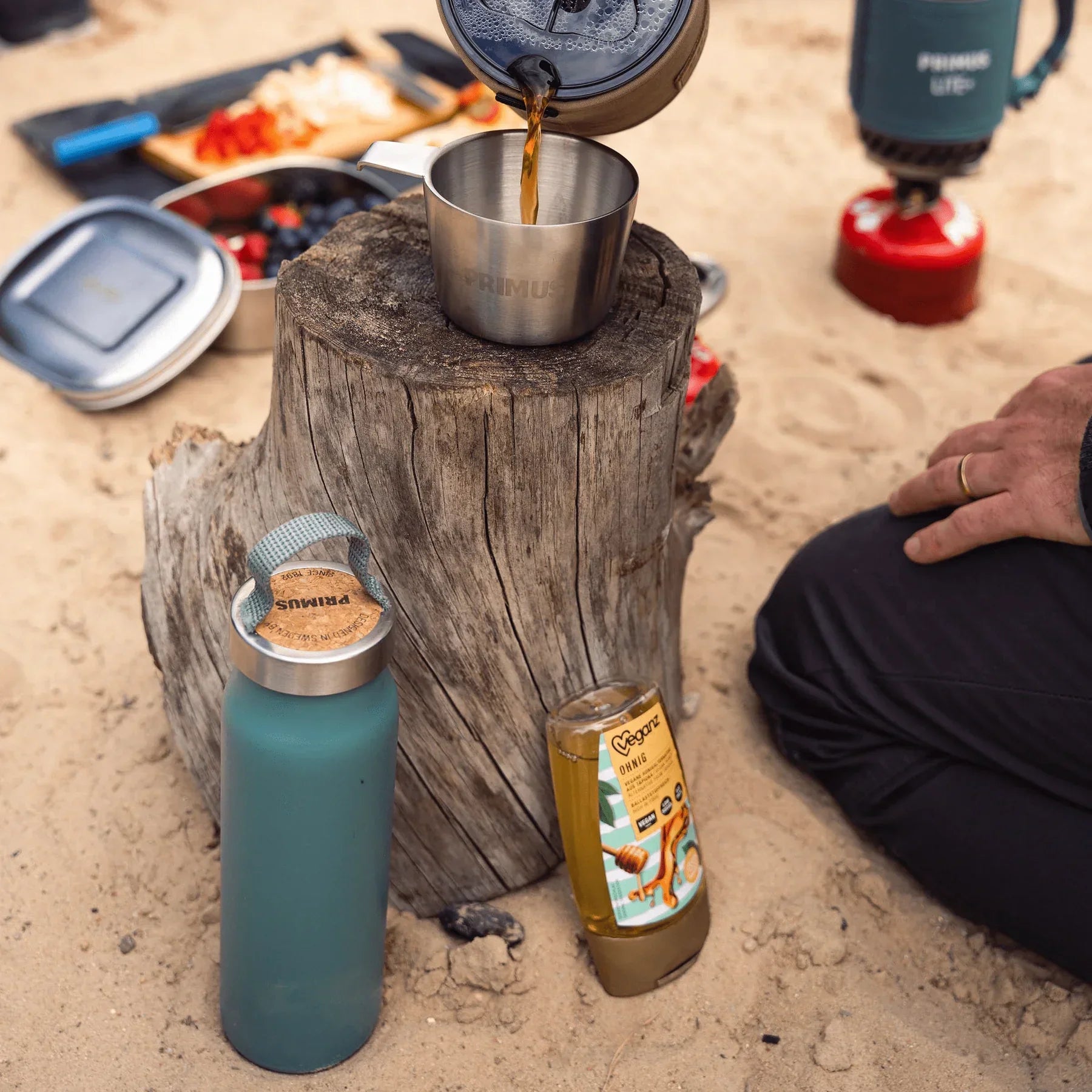 Klunken bottle in frost green and stainless cup on tree stump at sandy outdoor picnic